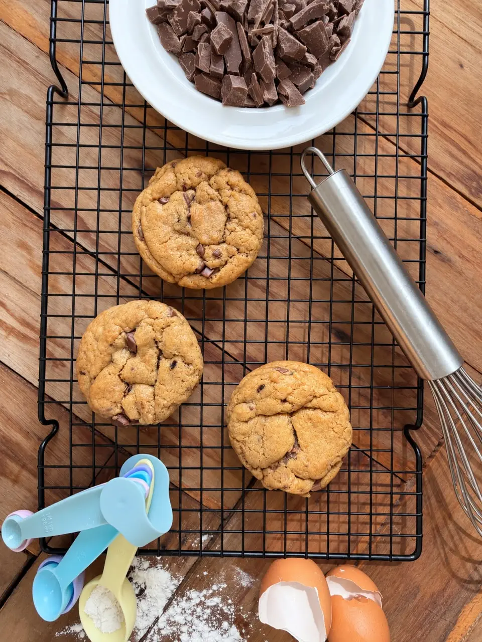 Three choc chip cookies stacked on a wooden board